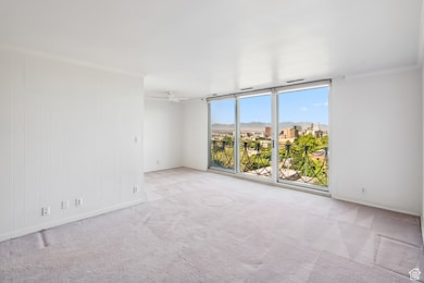 Carpeted empty room featuring a wall of windows, ornamental molding, and ceiling fan