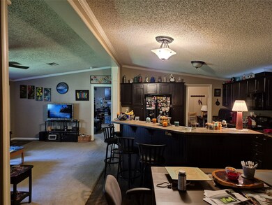 Kitchen featuring ornamental molding, vaulted ceiling, a textured ceiling, carpet floors, and a kitchen bar