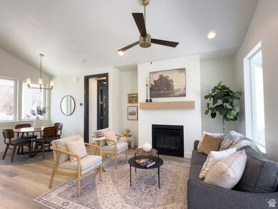 Living room featuring light wood-style flooring, a chandelier, a large fireplace, lofted ceiling, and a ceiling fan