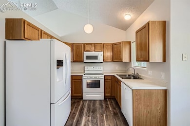 Kitchen featuring white appliances, vaulted ceiling, a textured ceiling, a sink, and brown cabinets