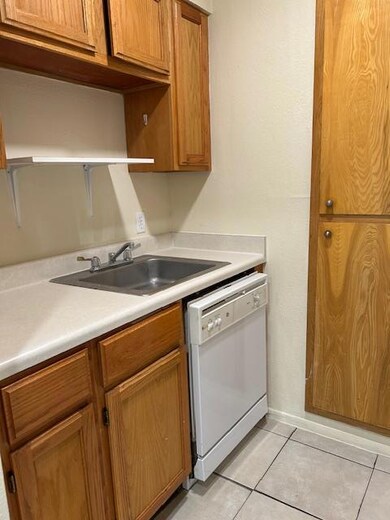 Kitchen featuring open shelves, light tile patterned floors, light countertops, a sink, and dishwashing machine