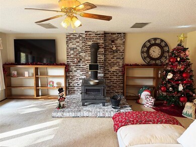 Carpeted living room with a wood stove, a textured ceiling, and ceiling fan