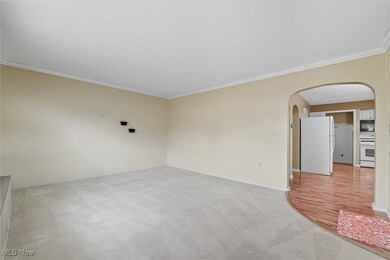 Unfurnished room with arched walkways, ornamental molding, and light carpet