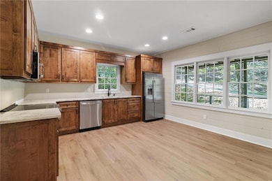 Kitchen with wood cabinetry, appliances with stainless steel finishes, recessed lighting, light wood finished floors, and light stone counters
