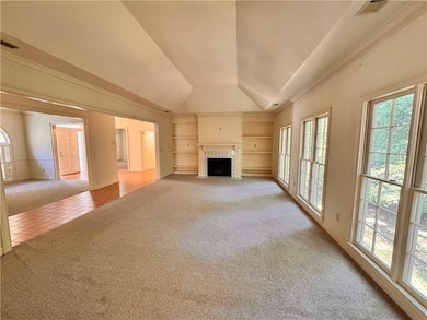 Unfurnished living room featuring light carpet, built in features, lofted ceiling, a fireplace with flush hearth, and light tile patterned floors
