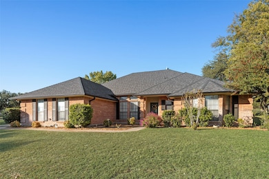 View of front facade with brick siding, a front yard, and roof with shingles