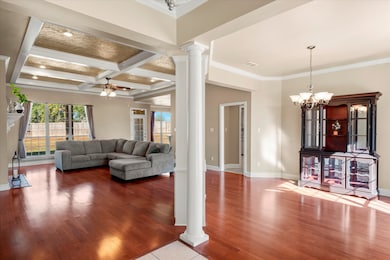 Living area with crown molding, coffered ceiling, light wood-style flooring, beamed ceiling, and a chandelier