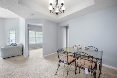 Dining space with light carpet, a tray ceiling, a chandelier, and a textured ceiling