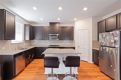Kitchen with appliances with stainless steel finishes, backsplash, dark brown cabinets, a kitchen island, and recessed lighting