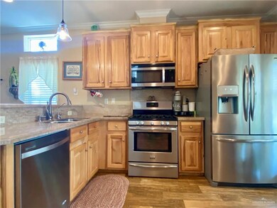 Kitchen with pendant lighting, sink, appliances with stainless steel finishes, light hardwood / wood-style flooring, and light stone countertops