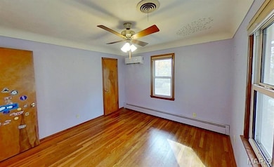 Unfurnished room featuring baseboard heating, light wood-style flooring, a ceiling fan, and an AC wall unit