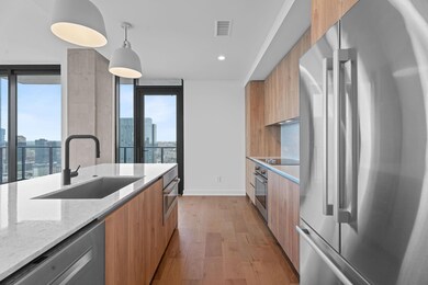 Kitchen with stainless steel appliances, modern cabinets, light wood-style floors, light stone counters, and a city view