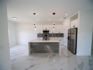 Kitchen featuring appliances with stainless steel finishes, a center island with sink, pendant lighting, light stone countertops, and backsplash