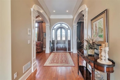 Foyer with arched walkways, wood finished floors, visible vents, and ornate columns
