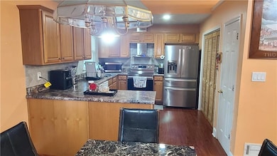 Kitchen featuring stainless steel appliances, dark wood-style floors, tasteful backsplash, hanging light fixtures, and brown cabinetry