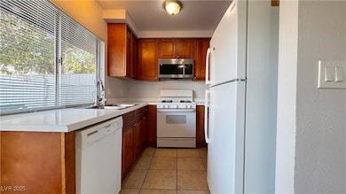 Kitchen featuring brown cabinets, white appliances, light countertops, and light tile patterned floors