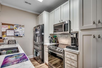 Kitchen with stainless steel appliances, ornamental molding, decorative backsplash, light wood-style floors, and white cabinets