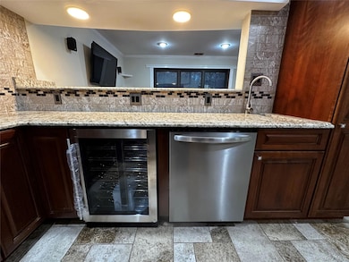Kitchen with cherry wood cabinets, wine cooler, stainless steel dishwasher, granite countertops, and ornamental molding