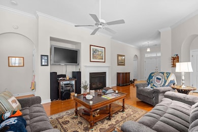 Living area featuring arched walkways, wood finished floors, ceiling fan, crown molding, and baseboards