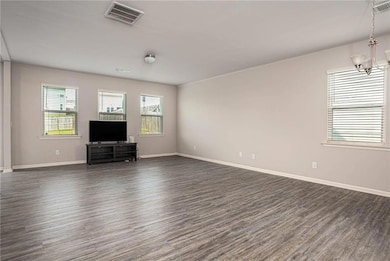 Unfurnished living room featuring dark wood-style flooring, a chandelier, and baseboards