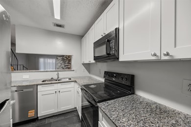 Kitchen with black appliances, white cabinetry, light stone countertops, and a textured ceiling