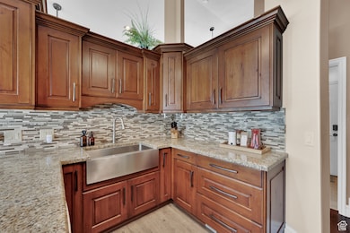 Kitchen featuring light stone countertops, tasteful backsplash, brown cabinets, and light wood finished floors