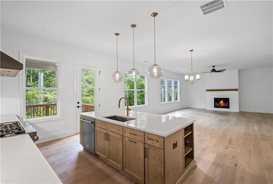 Kitchen featuring a sink, dishwasher, open shelves, light wood finished floors, and a lit fireplace