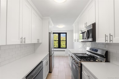 Kitchen featuring stainless steel appliances, white cabinetry, radiator, and light stone counters