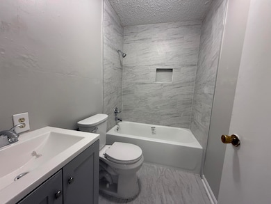 Bathroom featuring a textured ceiling, toilet, bathing tub / shower combination, vanity, and marble finish floor