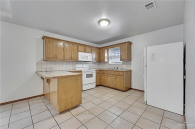 Kitchen with tile countertops, tasteful backsplash, white appliances, and light tile floors