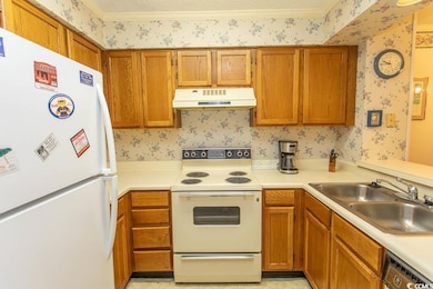 Kitchen featuring white appliances, under cabinet range hood, wallpapered walls, a sink, and light countertops