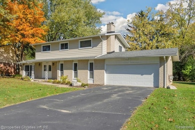 Traditional home featuring a front lawn, a porch, an attached garage, driveway, and a chimney