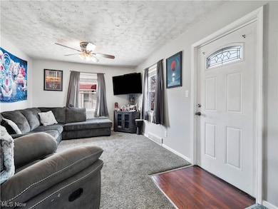 Living room with a textured ceiling, dark colored carpet, and ceiling fan