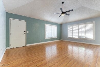 Unfurnished living room with a textured ceiling, light wood finished floors, vaulted ceiling, and a ceiling fan