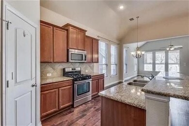 Kitchen with decorative light fixtures, dark hardwood / wood-style floors, ceiling fan with notable chandelier, appliances with stainless steel finishes, and lofted ceiling