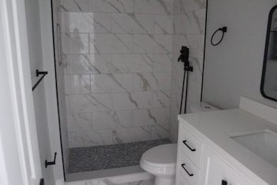 Full bath with vanity, tiled shower, and light marble finish flooring