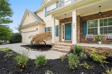 View of exterior entry featuring covered porch, stone siding, driveway, and an attached garage