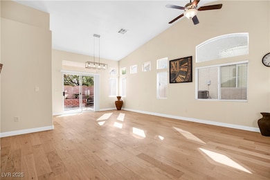 Unfurnished living room with light wood finished floors, high vaulted ceiling, a ceiling fan, and a chandelier