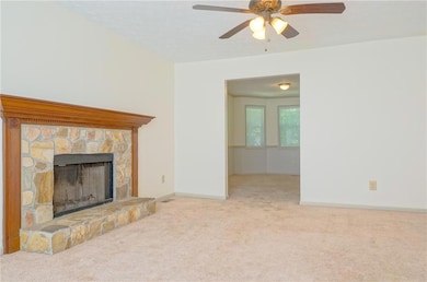 Unfurnished living room featuring carpet floors, a stone fireplace, ceiling fan, and baseboards