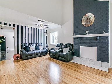 Living area with wood finished floors, ceiling fan, a brick fireplace, and a high ceiling