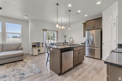 Kitchen featuring appliances with stainless steel finishes, decorative light fixtures, dark stone countertops, recessed lighting, and light wood finished floors