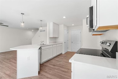 Kitchen with a peninsula, white cabinetry, appliances with stainless steel finishes, hanging light fixtures, and light wood-type flooring