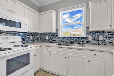 Kitchen with white appliances, crown molding, light countertops, and backsplash