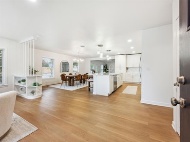 Kitchen with white cabinets, a center island with sink, light wood-type flooring, recessed lighting, and decorative light fixtures