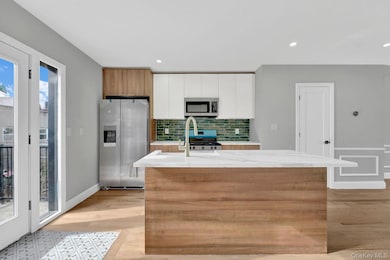 Kitchen featuring appliances with stainless steel finishes, decorative backsplash, a center island with sink, light stone counters, and white cabinets
