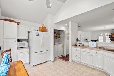 Kitchen featuring white cabinets, white appliances, washer and dryer, a chandelier, and light countertops