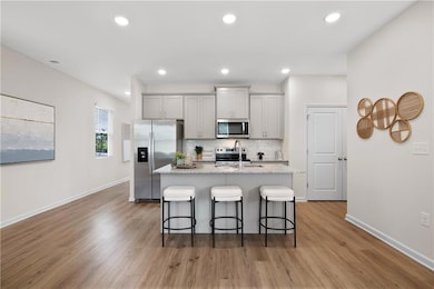 Kitchen featuring gray cabinetry, stainless steel appliances, a kitchen breakfast bar, recessed lighting, and light stone countertops