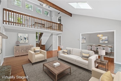 Living area featuring wood finished floors, a skylight, high vaulted ceiling, stairway, and beam ceiling