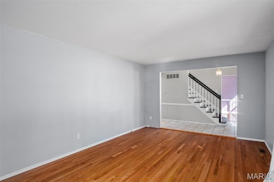 Unfurnished room with wood finished floors, stairway, and a chandelier