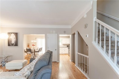 Living area with ornamental molding, light wood finished floors, a chandelier, and stairway